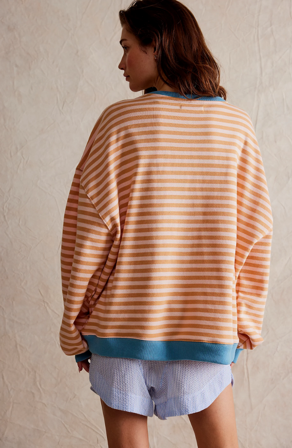 Vrouw in gestreepte trui met oranje en witte strepen, blauwe boorden, en lichtblauwe korte broek. Modieuze dameskleding, casual stijl.