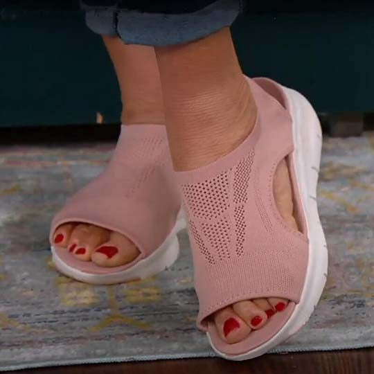 Roze open teen sandalen met ademend mesh ontwerp en witte zool, gedragen door een persoon op een tapijt. Comfortabele zomerschoenen voor dames.