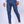 Man in blauwe slim-fit broek en witte sneakers, staand tegen een neutrale achtergrond. Modieuze herenmode, casual en stijlvol.