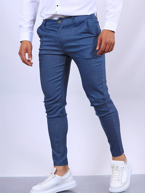Man in blauwe slim-fit broek en witte sneakers, staand tegen een neutrale achtergrond. Modieuze herenmode, casual en stijlvol.