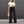 Vrouw in zwarte flared broek en witte crop top, met beige handtas, tegen grijze achtergrond. Modieuze dameskleding, casual stijl.