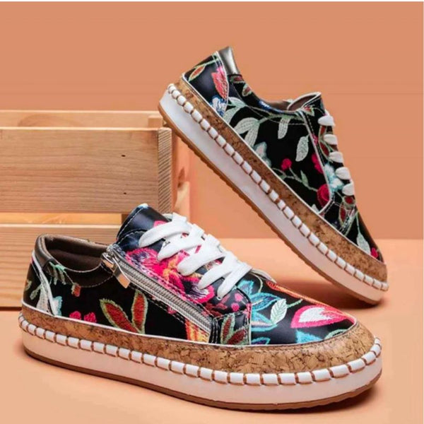 Zwarte sneakers met kleurrijke bloemenprint, witte veters en kurken zool, tegen een houten achtergrond. Trendy damesschoenen, casual stijl.