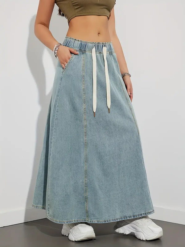 Vrouw in denim maxi rok met elastische tailleband en witte trekkoorden, gecombineerd met een crop top en sneakers. Trendy casual damesmode.