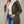 Vrouw in groene gewatteerde jas met capuchon, witte coltrui en blauwe jeans. Modieuze winterkleding, casual stijl, damesmode.