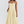 Vrouw in elegante gele midi-jurk met spaghettibandjes en geplooide rok, perfect voor zomermode en casual chique gelegenheden.
