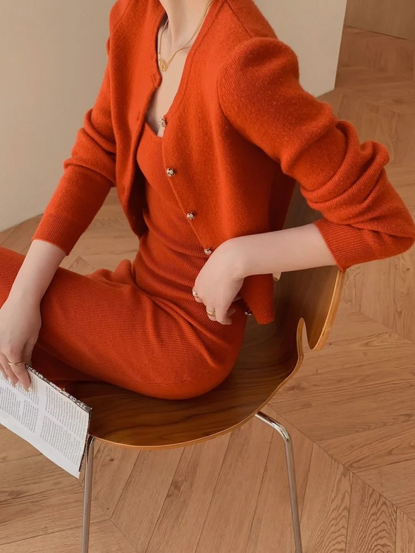 Vrouw in stijlvolle oranje gebreide jurk en vest, zittend op houten stoel, met tijdschrift. Mode, herfstkleding, elegantie, binnenhuis.