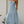 Vrouw in lichtblauwe zomerjurk met halternek, staand in tuin. Elegante maxi-jurk, perfect voor zomerse evenementen en casual stijl.