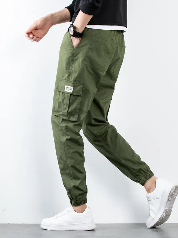 Man in groene cargo broek met elastische enkels en zijzakken, draagt witte sneakers. Casual herenkleding, comfortabele streetwear stijl.