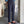 Man in blauwe blouse en stropdas draagt stijlvolle, donkergrijze pantalon met opgerolde zoom en bruine loafers. Moderne herenmode, zakelijke outfit.