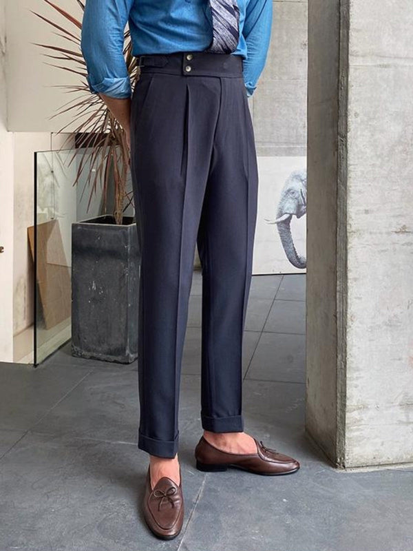 Man in blauwe blouse en stropdas draagt stijlvolle, donkergrijze pantalon met opgerolde zoom en bruine loafers. Moderne herenmode, zakelijke outfit.