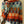 Vrouw in kleurrijke geruite trui met hoge kraag, oranje, blauw en groen tinten, draagt een bruine schoudertas. Modieuze herfstkleding.