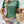 Vrouw in groene T-shirt met pofmouwen, denim shorts en gevlochten handtas. Trendy zomeroutfit, casual mode, accessoires, boho-stijl.