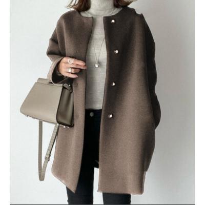 Bruine wollen jas met knopen, gedragen over een grijze coltrui. Vrouw houdt een stijlvolle beige handtas vast. Modieuze herfst- of winterkleding.