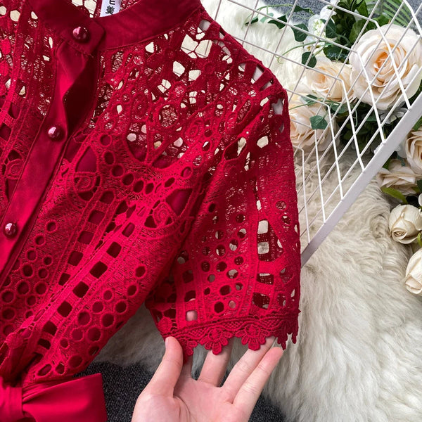 Rode kanten blouse met knoopsluiting en korte mouwen, gedetailleerd opengewerkt patroon, op een witte achtergrond met bloemen. Perfect voor elegante mode.