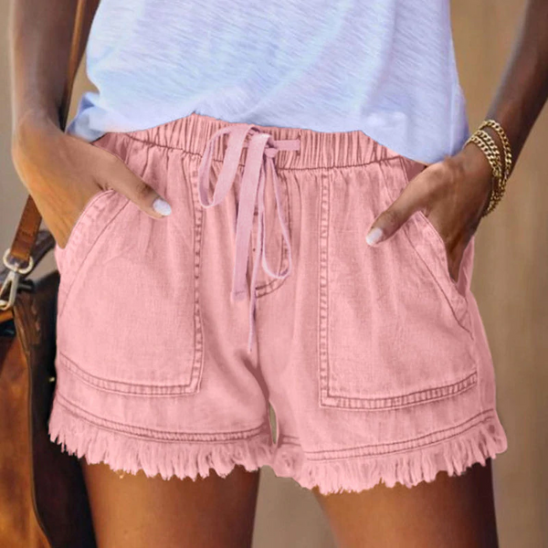 Vrouw draagt roze katoenen shorts met ruches en elastische tailleband, gecombineerd met een lichtblauw T-shirt. Zomermode, casual dameskleding.