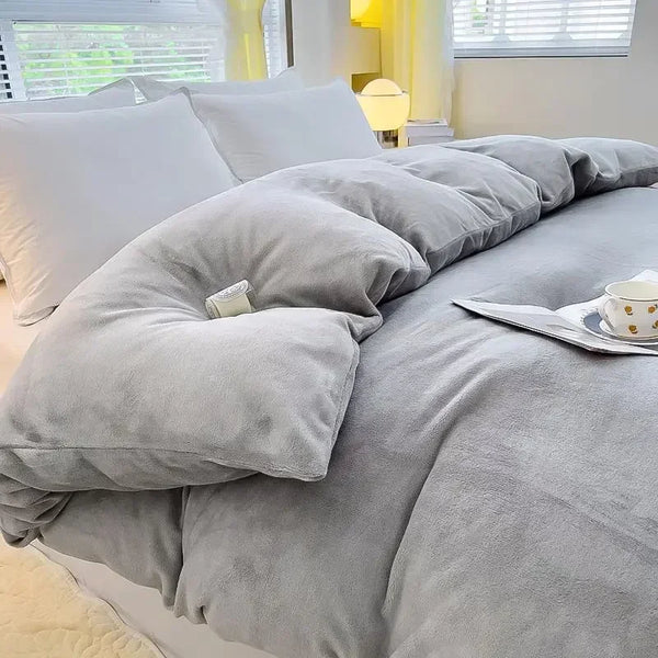 Grijze flanellen dekbedovertrek op een bed met witte kussens, kopje thee en tijdschrift, in een lichte slaapkamer met raam en lamp.