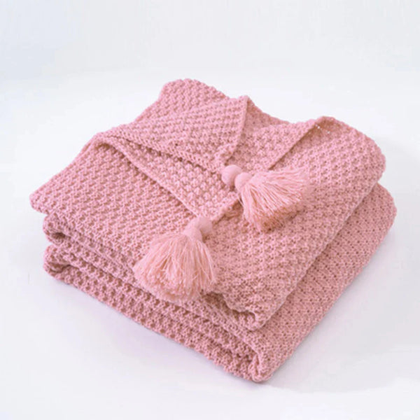 Gevouwen roze gebreide deken met kwastjes, zachte textuur, perfect voor interieurdecoratie en comfort. Ideaal voor slaapkamer of woonkamer styling.
