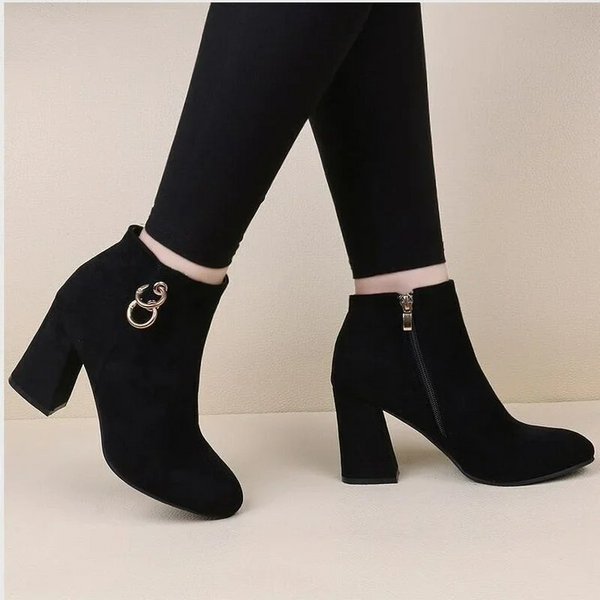 Zwarte suède enkellaarsjes met hoge hak en ritssluiting, versierd met metalen ringdetail. Stijlvolle damesmode, perfect voor herfst- en winteroutfits.