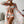 Vrouw in kleurrijke strandoutfit met abstract patroon, bestaande uit bikini, shorts en kimono, poseert met brede hoed in moderne woonkamer.