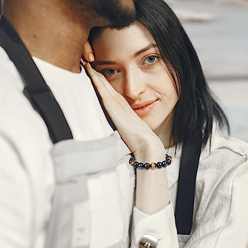 Vrouw met zwart haar draagt een armband met blauwe en gouden kralen, leunt tegen man in witte schort. Stijlvolle sieraden, intieme sfeer.