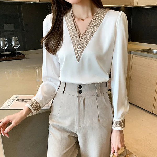 Elegante vrouw in witte blouse met V-hals en beige broek, staand in moderne keuken. Mode, dameskleding, stijlvolle outfit, casual chic.