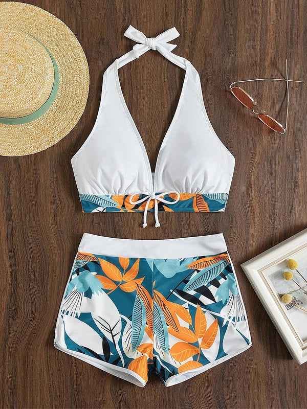 Dames bikini set met tropische print, haltertop en hoge taille shorts op houten achtergrond. Inclusief zonnebril en strohoed. Perfect voor strandmode.