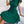 Groene geplooide jurk met strikdetail, gedragen door zittende vrouw op bank. Elegante damesmode, zomerjurk, casual chic stijl.