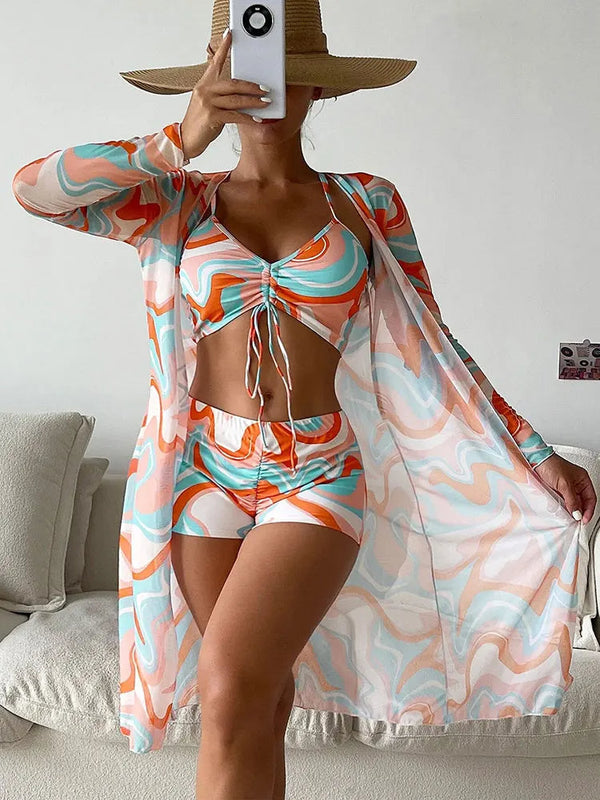 Vrouw in kleurrijke strandoutfit met abstract patroon, bestaande uit bikini, shorts en kimono. Zomerse mode, trendy strandkleding, stijlvolle hoed.