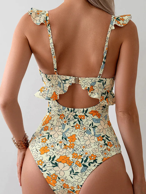 Vrouw in bloemenbadpak met ruches, rugsluiting en oranje bloemenprint. Trendy damesmode, zomerstrandkleding, stijlvolle badmode.