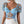 Vrouw draagt blauwe kanten crop top met bloemenpatroon en pofmouwen, gecombineerd met witte broek. Trendy damesmode, zomeroutfit, elegante stijl.