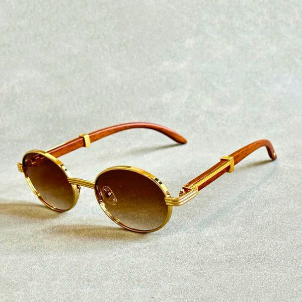 Gouden ronde zonnebril met bruine glazen en houten pootjes op grijze achtergrond. Luxe vintage design, modieuze accessoires, unisex stijl.