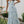 Vrouw in lange, blauwe bloemenjurk poseert buiten naast tafel met rozen; zomermode, elegante maxi-jurk, tuinfeest outfit.