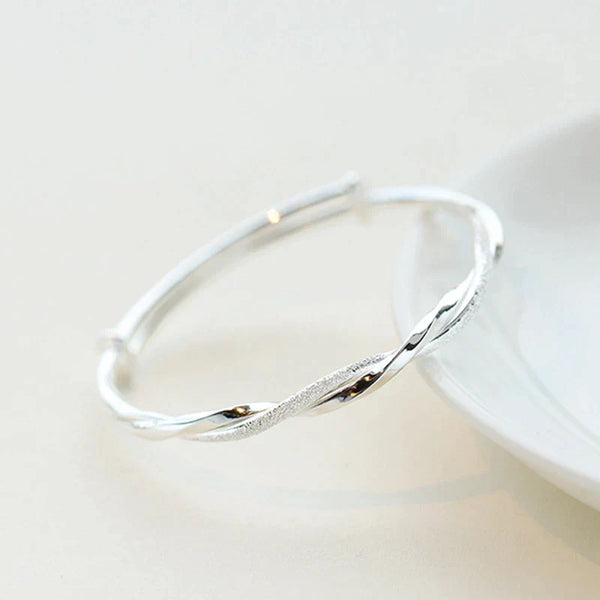 Zilveren armband met gedraaide details op witte achtergrond, elegant en modern design, perfect voor dames, sieradenaccessoire.