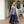 Vrouw in grijze cardigan en lange rok loopt voor winkel, modieuze herfstoutfit, casual stijl, houten vloer, plantenpot op achtergrond.