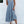 Vrouw in lichtblauwe zomerjurk met knopen, staand tegen witte muur. Casual mode, boho-stijl, sandalen. Perfect voor zomerse dagen.