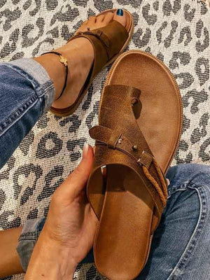 Bruine leren sandalen met gesp, gedragen door persoon in blauwe jeans op luipaardprint tapijt. Comfortabele zomerschoenen voor dames.
