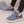 Grijze geribbelde pantoffels met witte voering, gedragen door persoon in zwarte jeans. Comfortabele winterse huisschoenen voor dames.