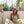 Vrouw in groene zomerjurk zit op balkon met bloemen en picknickmand, omgeven door groen en zonlicht. Perfect voor mode- en lifestyle-inspiratie.
