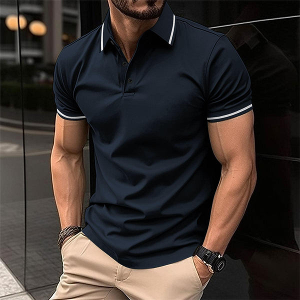 Man in donkerblauw poloshirt met witte accenten, beige broek, horloge en armband. Stijlvolle herenkleding, casual mode, stedelijke achtergrond.