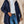 Vrouw in blauwe gewatteerde jas met capuchon, witte coltrui en jeans. Modieuze winterkleding, casual stijl, buitenmuur achtergrond.