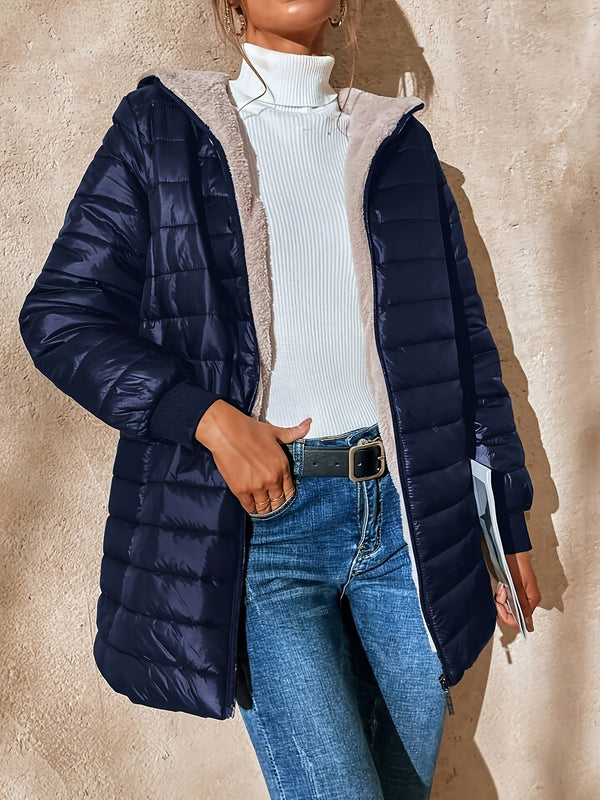 Vrouw in blauwe gewatteerde jas met capuchon, witte coltrui en jeans. Modieuze winterkleding, casual stijl, buitenmuur achtergrond.