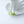 Twee zilveren kettingen met avocado-hangers, elk met een hartvormig detail, op een witte kop en schotel. Perfecte sieraden voor avocado-liefhebbers.