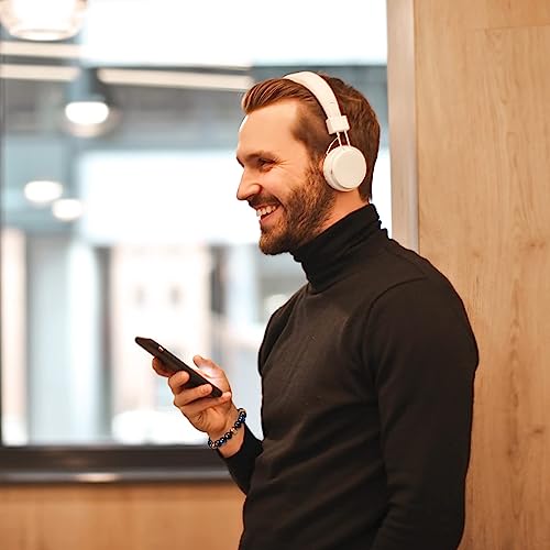 Man met koptelefoon en smartphone, glimlachend in moderne kantooromgeving. Technologie, muziek luisteren, mobiele communicatie.