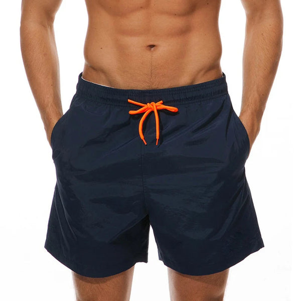 Donkerblauwe zwembroek met oranje trekkoord, gedragen door een man. Perfect voor strandmode en zomerse activiteiten. Comfortabel en stijlvol ontwerp.