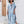 Vrouw in blauwe en witte gestreepte kaftan jurk, staand voor houten deur en bloemen. Zomermode, casual strandkleding, comfortabele damesjurk.