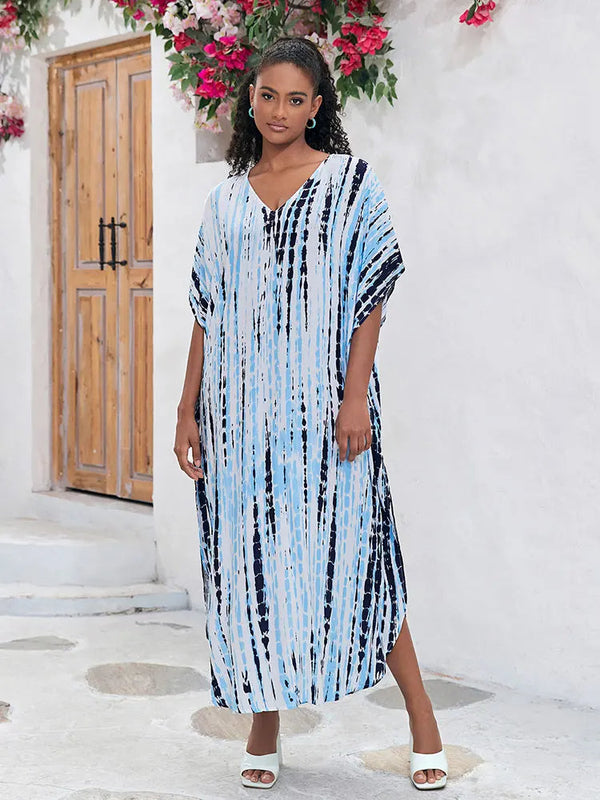 Vrouw in blauwe en witte gestreepte kaftan jurk, staand voor houten deur en bloemen. Zomermode, casual strandkleding, comfortabele damesjurk.