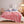 Roze fleece deken op bed met witte rand, omgeven door kussens en nachtkastje met lamp. Gezellige slaapkamerinrichting, modern interieur.