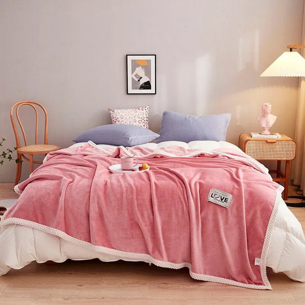 Roze fleece deken op bed met witte rand, omgeven door kussens en nachtkastje met lamp. Gezellige slaapkamerinrichting, modern interieur.