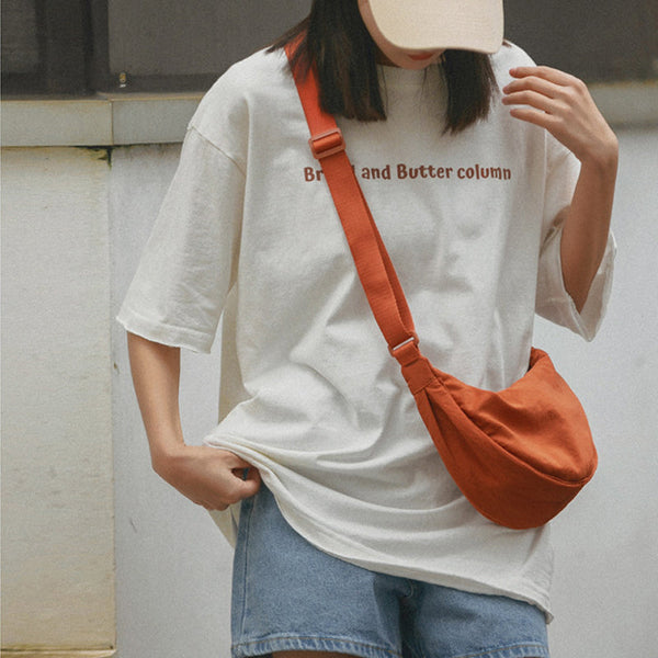 Vrouw in casual outfit met witte oversized T-shirt met tekst, oranje schoudertas en spijkershorts. Mode, streetwear, zomerkleding.