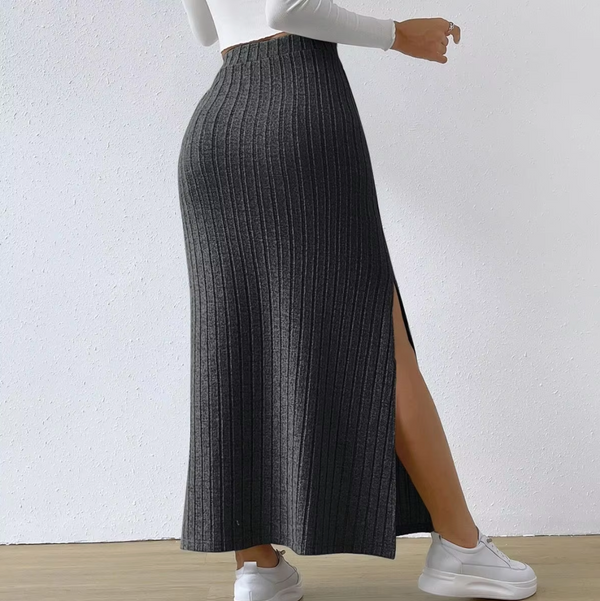 Grijze geribbelde maxi-rok met hoge taille en zijsplit, gedragen door een vrouw in witte sneakers en een witte top, tegen een witte achtergrond.